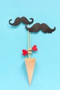 Couple paper mustache props on stick fastened clothespin heart in ice cream waffle cone on blue background. Concept Homosexuality Royalty Free Stock Photo