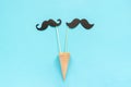 Couple paper mustache props on stick in ice cream waffle cone on blue background. Concept Homosexuality gay love. International Royalty Free Stock Photo