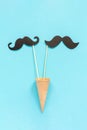 Couple paper mustache props on stick in ice cream waffle cone on blue background. Concept Homosexuality gay love. International