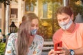 Couple at the park using the smartphone, wearing face masks and respecting social distancing during a pandemic