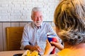 Couple of pensioners eating together at fast food or restaurant - seniors meeting in their first date clinking withg the cup - man Royalty Free Stock Photo