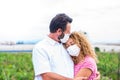 Couple of people hugged together and man giving a kiss at his wife - two adults wearing medical and surgical mask on them face to