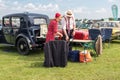 Couple in period dress setting up a picnic behind classic vintage car