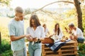 Couple with phone against people at background. Group of young people have vacation outdoors in the forest. Conception of weekend