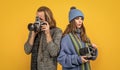 Couple of photojournalists hold photo cameras taking photograph yellow background, paparazzi