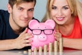 Couple With Piggybank And Stack Of Coins At Desk