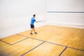 Man is preparing to hit squash ball on front wall inside court, with blue service line Royalty Free Stock Photo