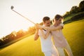 Couple playing golf together at sunset, swinging together to hit the ball with a golf club Royalty Free Stock Photo