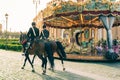 Couple of police on horseback passing by a carousel in the city of Rome. Warm, soft and orange colors.
