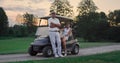 Couple posing golf cart outside. Two golfers take clubs sport equipment on field Royalty Free Stock Photo