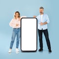 Couple Posing With Smartphone Pointing Fingers At Screen, Blue Background Royalty Free Stock Photo