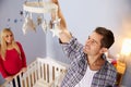 Couple With Pregnant Wife Hanging Mobile In Nursery