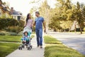 Couple Push Daughter In Stroller As They Walk Along Street Royalty Free Stock Photo