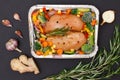 Raw chicken breasts or fillet in metal container with ingredients on black background