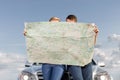 Couple reading map while leaning on car hood during road trip