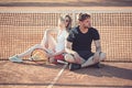 Couple relax on tennis court after training. Sportsman and sportswoman sit at net. Tennis players rest on clay surface
