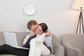 Couple resting on couch using laptop. Married couple having some relaxed time on sofa at home. Man kissing his Royalty Free Stock Photo