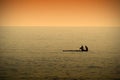 A couple resting while paddleboarding in a calm sea at sunset time.