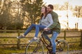 Couple Riding Bike Through Countryside With Woman Sitting On Handlebars