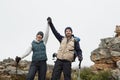 Couple on rocky landscape with hands raised against sky