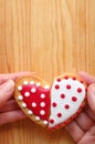 Couple`s hands holding two half heart shaped cookies attach on wooden background Royalty Free Stock Photo
