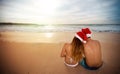 Couple with Santa hats sitting on sandy beach Royalty Free Stock Photo