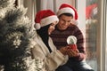 Couple in Santa hats with snow globe near window Royalty Free Stock Photo