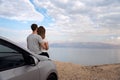 Couple seated on the engine hood of a rented car on a road trip in israel