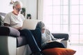 Couple of seniors at home - man with laptop and glasses sitting at the sofa - woman sitting on the grund reading a book - indoor Royalty Free Stock Photo