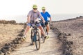 Couple of seniors at mountains or park riding a bikes together with open legs - mature people having fun together - beach and sea