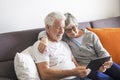 Couple of seniors smiling and looking at the same tablet hugged on the sofa - indoor, at home concept - caucasians mature and Royalty Free Stock Photo