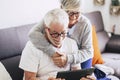 Couple of seniors smiling and looking at the tablet - woman hogging at man with love on the sofa - indoor Royalty Free Stock Photo