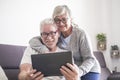 Couple of seniors smiling and looking at the tablet - woman hogging at man with love on the sofa - indoor - showing Royalty Free Stock Photo