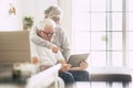 Couple of seniors smiling and looking at the tablet - woman hogging at man with love on the sofa - indoor - showing Royalty Free Stock Photo