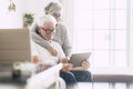 Couple of seniors smiling and looking at the tablet - woman hogging at man with love on the sofa - indoor Royalty Free Stock Photo