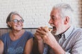 Couple of seniors together having fun eating and laughing - mature man holding an hamurger and eating it with mouth opened and his