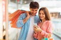 Couple Shopping Online Using Smartphone Posing Holding Bags In Mall Royalty Free Stock Photo