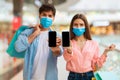 Couple On Shopping Showing Smartphones Wearing Masks In Modern Mall