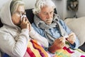 Couple of sicks seniors and mature people sitting at the sofa with fever looking at the thermometer with high temperature - two Royalty Free Stock Photo