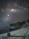 Couple sit on beach using flashlight point to milky way.