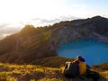 A couple sit watching an awesome sunrise together in front of the blue crater lake of Kelimutu volcano, Flores