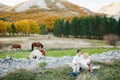 Couple sits hugging each other on a blanket on the lawn in the autumn forest. Horses graze in the background Royalty Free Stock Photo