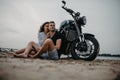 Couple sits and hugs on beach near motorcycle