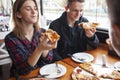 Couple sits in a pizzeria and eats pizza, a guy and a girl dine fast food, smile and relax in a restaurant