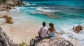A couple sits side by side on a large boulder backs facing the camera as they watch the crystal clear waves crash Royalty Free Stock Photo