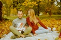 Couple sitting on autumn fallen leaves in a park, enjoying a beautiful autumn day. Happy joyful young family father, mother and Royalty Free Stock Photo