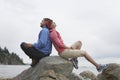 Couple Sitting Back To Back On Rocks Against Ocean Royalty Free Stock Photo