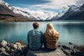 Couple sitting on a bench in front of a lake and looking at the mountains, rear view of Travelers couple looking at the mountain Royalty Free Stock Photo