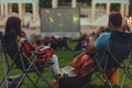 couple sitting in camp-chairs in city park looking movie outdoors at open air cinema