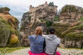 Meteora - Couple sitting on cliff edge with scenic view of Holy Monastery of Great Meteoron appearing from fog, Kalambaka, Meteora Royalty Free Stock Photo